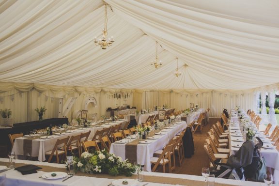 Wedding marquee interior with wooden chairs and long banqueting tables in Hartley Witney, Hampshire.